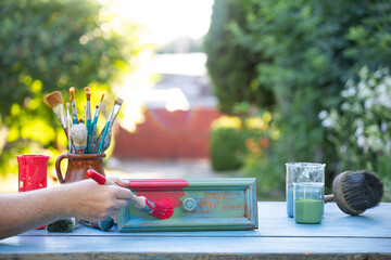 Woman painting a wooden furniture outdoors, an eco-friendly re-use business.