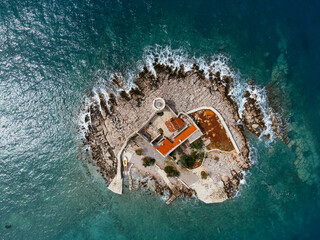 Aerial shot of rocky islet with red roofed building in Montenegro surrounded by turquoise Adriatic...