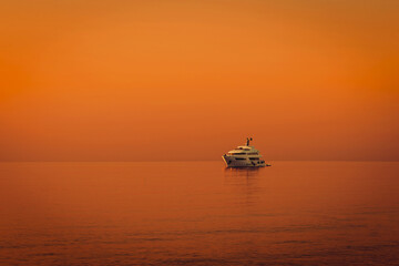 Luxury yacht floats on calm sea under deep orange sunset sky. Peaceful ocean scene perfect for...