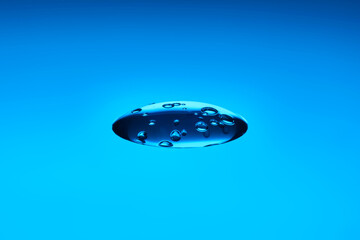 A drop of cosmetic product or serum on a blue background.