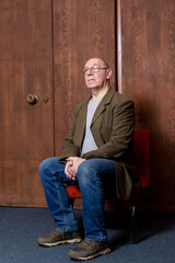 A middle-aged man in a green jacket sits by an old wooden door