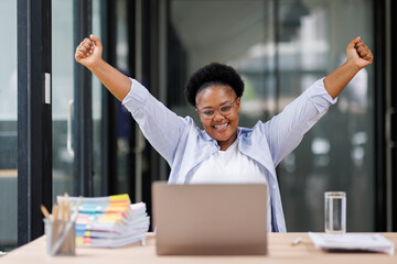 Excited cheerful Black african american woman using laptop computer on sofa at workplace, getting good news, feeling joy, dancing with hands, singing, laughing, making winner gesture, happy to win pri