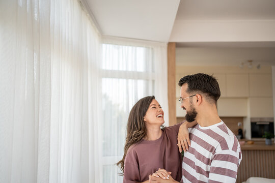 Happy couple holding hands and laughing together at home - Powered by Adobe