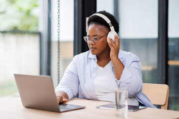 Young creative business African American woman working on digital tablet while wearing headphones...