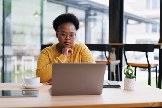 Young black female entrepreneur concentrating on her laptop in a bright and modern cafe, enjoying a cup of coffee while managing her business remotely