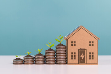 A sustainable house model with a solar panel and stacked coins topped with soil and green plants,...