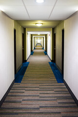 Modern inn hotel motel empty long corridor with carpet floor design and lamps lights illuminated vertical interior view of building architecture