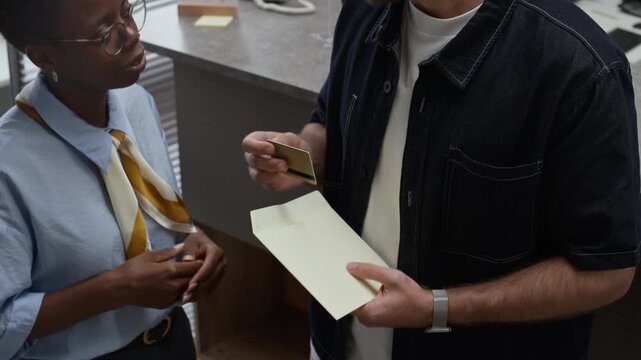 Tilt up shot of male Caucasian client taking card out of envelope while communicating with black female bank manager in office