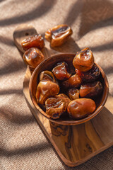 Wooden bowl of dates on wooden board with several dates scattered in the background