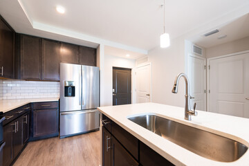 Empty kitchen modern apartment house home with sink faucet quartz countertop island by new fridge refrigerator wood cabinets and recessed ceiling lamp light