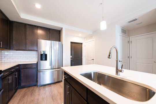 Empty kitchen modern apartment house home with sink faucet quartz countertop island by new fridge refrigerator wood cabinets and recessed ceiling lamp light