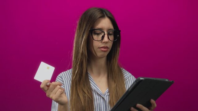 Woman wearing glasses holding creditcard to tablet touchscreen in pink studio; digital security trust. - Powered by Adobe