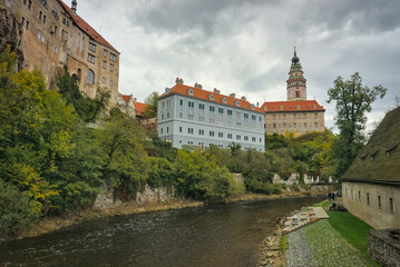 Obraz premium Český Krumlov, Czech Republic: River flowing past historic buildings and castle on a cloudy day.