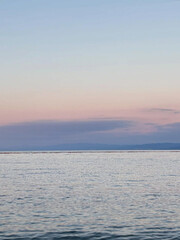 Calm ocean under pastel pink evening sky.