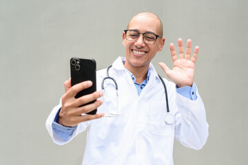 Hispanic Male Doctor in Lab Coat with Stethoscope on Plain Background Using Phone