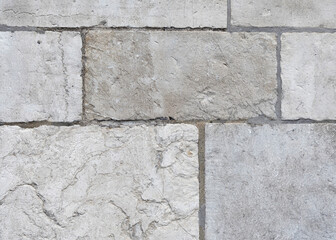 Old, weathered wall lined with large natural grey stones of various shapes with intricate textures, stones are laid with visible seams filled with mortar,