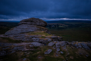 Family hiking on Dartmoor tors at sunset, silhouetted against dramatic skies in scenic moorland...