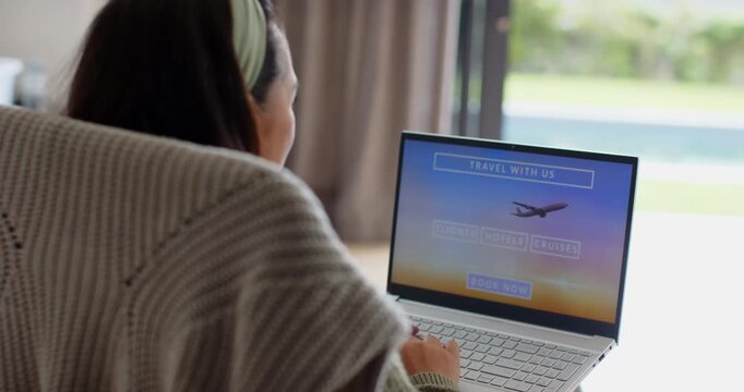 Asian woman opening laptop, typing on travel site to plan trip at home desk, copy space