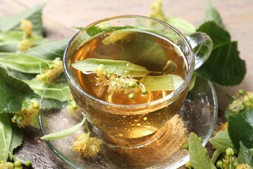 Tasty linden tea in cup, leaves and flowers on table, closeup