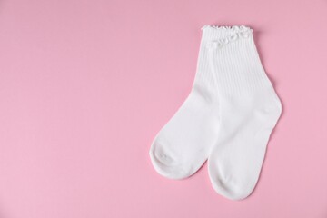 Pair of comfortable white socks on pink background, top view. Space for text