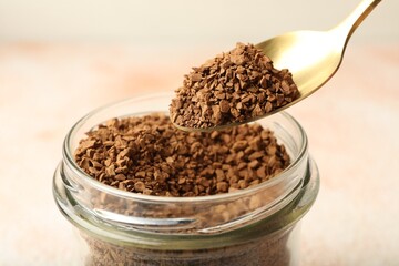 Taking granulated instant coffee from jar with spoon on blurred light background, closeup