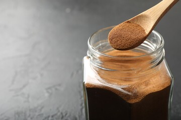 Adding instant coffee powder from spoon into jar on dark textured table, closeup. Space for text