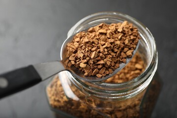 Spoon with granulated instant coffee and jar on dark table, closeup
