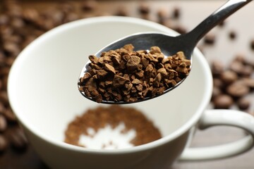 Spoon with instant coffee and cup on table, closeup