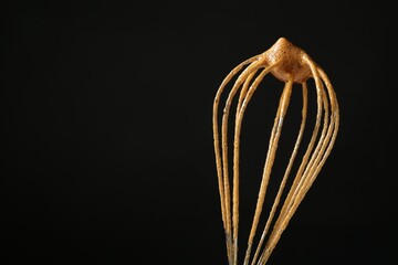 Making delicious dalgona coffee. Whisk with cream on black background, closeup. Space for text