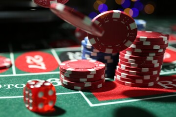 Casino chips and die falling on roulette table against blurred lights, closeup