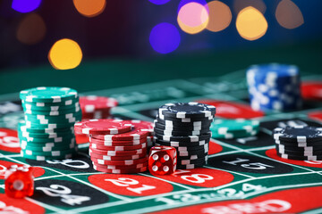 Casino chips and dice on roulette table against blurred lights, closeup