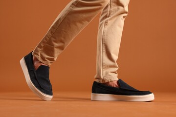 Man wearing pair of dark blue shoes on brown background, closeup