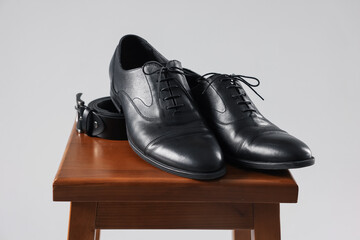 Pair of black leather shoes on stool against light background