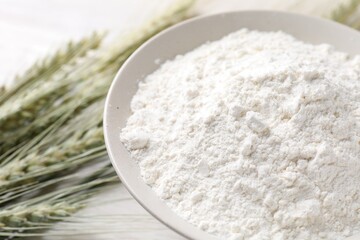Green wheat spikes and flour on light table, closeup