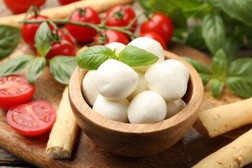 Tasty mozzarella cheese balls, tomatoes, basil and grissini on table, closeup