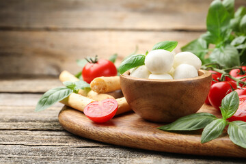 Tasty mozzarella cheese balls, tomatoes, basil and grissini on wooden table, closeup