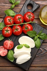 Tasty mozzarella cheese, tomatoes and basil on wooden table, top view
