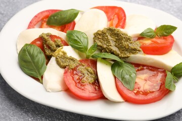 Tasty salad Caprese with mozzarella, tomatoes, basil and pesto sauce on grey table, closeup
