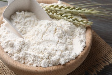 Flour in bowl and green wheat spikes on table, closeup