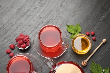 Aromatic raspberry tea in glass cups, teapot, berries, green leaves and honey on black table, flat...