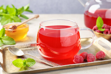 Tasty raspberry tea, berries, honey and mint on light grey table, closeup