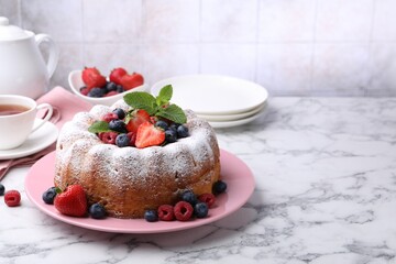 Tasty Bundt cake with powdered sugar and berries on white marble table, space for text