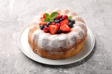 Tasty Bundt cake with powdered sugar and berries on grey textured table