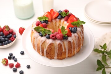 Delicious bundt cake with berries, glaze and mint on white wooden table, closeup
