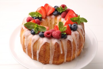 Delicious bundt cake with berries, glaze and mint on white table, closeup