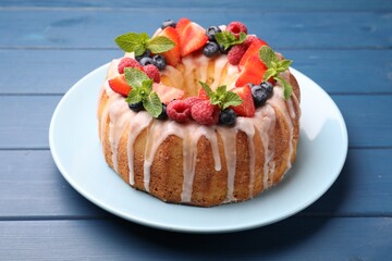 Delicious bundt cake with berries, glaze and mint on blue wooden table, closeup
