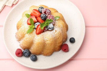 Delicious bundt cake with powdered sugar, berries and mint on pink wooden table, closeup