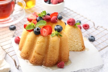 Tasty Bundt cake with berries, honey, mint and tea on light grey table, closeup