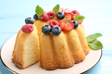Tasty Bundt cake with berries and mint on light blue wooden table, closeup
