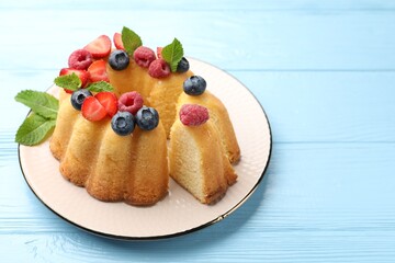 Tasty Bundt cake with berries and mint on light blue wooden table, closeup. Space for text